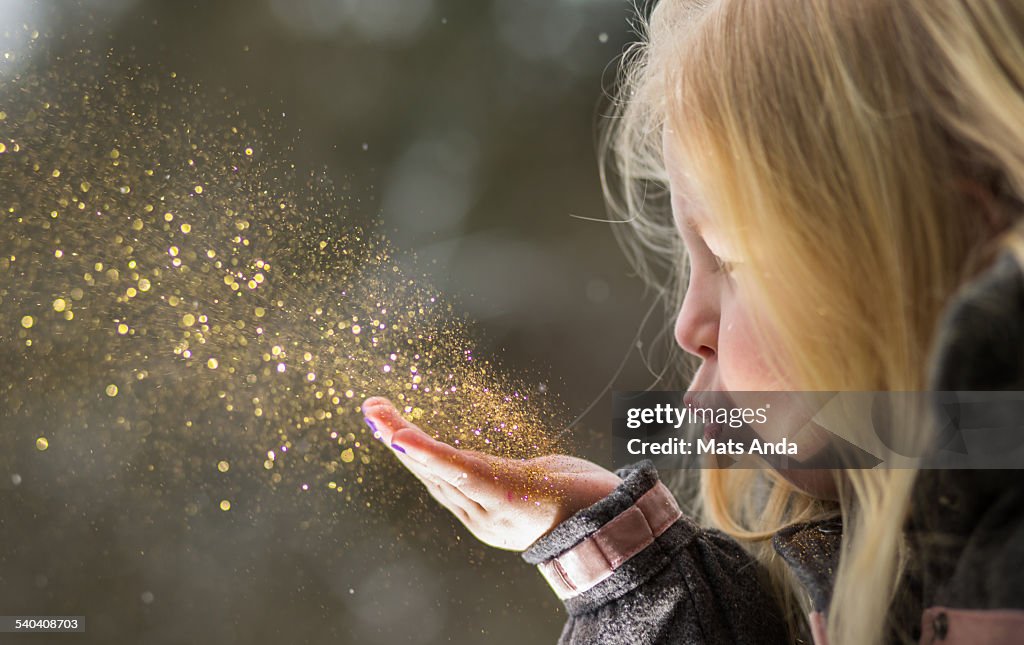 Young girl blows glitter into the air