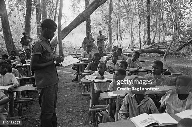 Teacher talks to his pupils at a guarded outdoor classroom during the Portuguese Colonial War, Guinea-Bissau, West Africa, 1972.