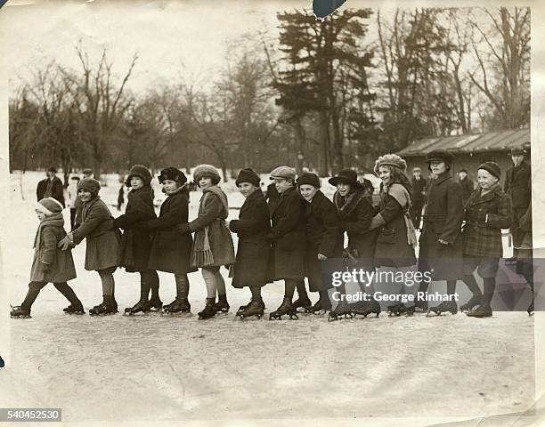 "Conga Line on Skates." Boys and girls are shown on ice skates, lined up one behind another and holding each other's waists. They are about to be off...