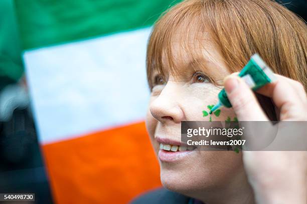 smiling woman having her face painted on st. patricks day. - st patricks day 2016 stock pictures, royalty-free photos & images