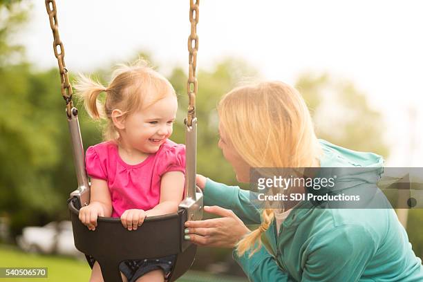 smiling toddler girl on swing with mother - nanny stock pictures, royalty-free photos & images