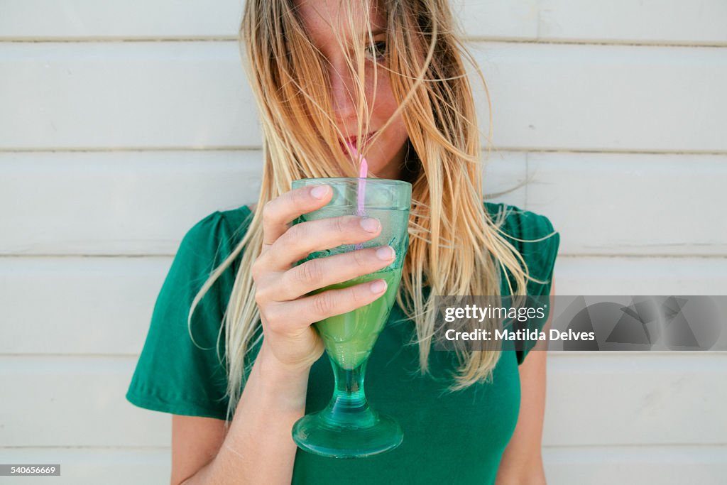 Young blond woman in a green top, drinking juice
