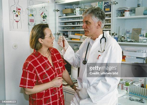Arztpraxis: im Labor hält ein Arzt ein gefülltes Reagenzglas in der Hand und erläutert seiner Patientin den Inhalt. Arztgespräch; Beratungsgespräch....