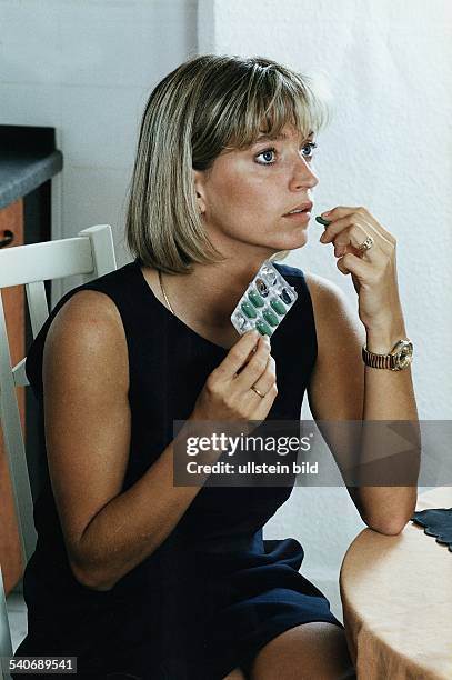 Eine Frau steckt sich eine Kapsel in den Mund, die sie einer Blister-Packung entnommen hat. Tabletteneinnahme. Undatiertes Foto, 1990er Jahre....