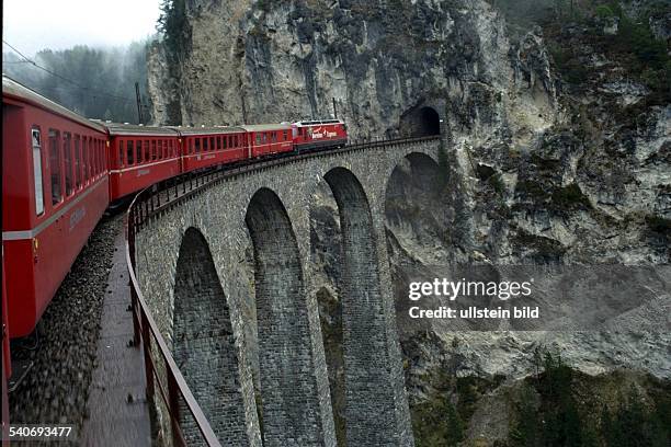 Landwasser-Viadukt in den Schweizer-Alpen: Ein Zug der Rhätischen Bahn fährt über die Eisenbahnbrücke in den Tunnel eines Berges. .
