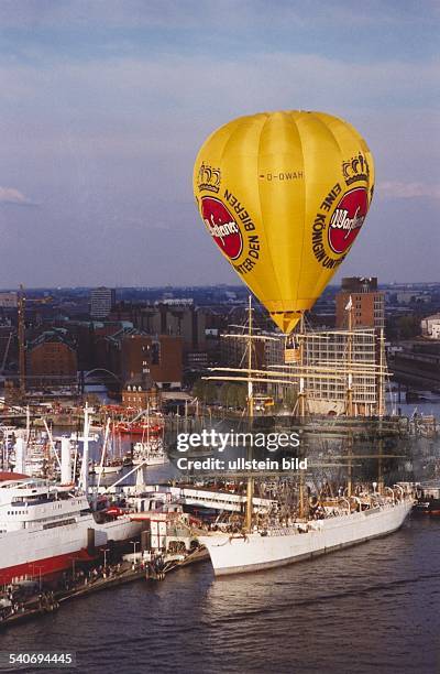 Ein gelber Heißluftballon mit der Warsteiner Werbung fährt über den Hamburger Hafen. Er scheint den Viermaster, der an der Überseebrücke festgemacht...