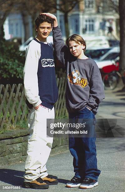 Zwei unterschiedlich große Jugendliche stehen nebeneinander. Beide tragen Sweat-Shirts, Sportschuhe und lange Hosen. Der linke Junge ist 14 Jahre alt...