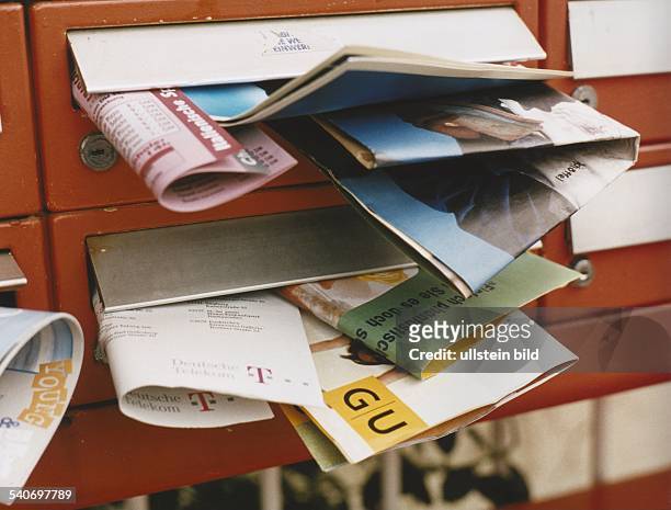 Überquellende Hausbriefkästen: Prospekte verschiedener Firmen hängen aus den Schlitzen mehrerer Briefkästen. .