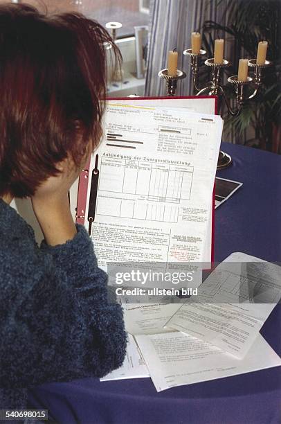 Eine Frau hält einen Aktenordner mit der Ankündigung einer Zwangsvollstreckung in der Hand. Auf dem Tisch liegen verschiedene Mahnungen. Symbolbild .