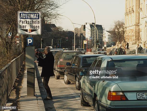 An einem Parkscheinautomat in der Hamburger Innenstadt löst eine Frau neben einer Reihe parkender PKWs einen Parkschein. Parkgebühr, Parkplatz,...