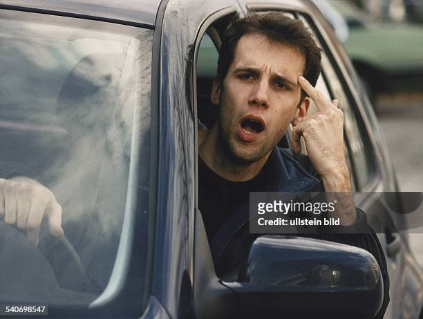 Nervöser Autofahrer tippt sich mit dem Zeigefinger an die Stirn. Aggression; Aggressivität; Mann; Nervosität; Straßenverkehr; Verkehrsverhalten;...