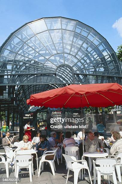 Gäste sitzen bei schönem Wetter unter einem Sonnenschirm an Tischen vor 'Rügi's Snack-Bar', einem Schnellrestaurant im Glaspavillon auf dem...