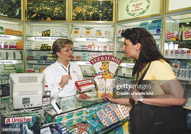 In einer Apotheke steht hinter dem Verkaufsthresen eine Apothekerin/Apothekenhelferin und führt ein Beratungsgespräch zum Medikament 'frubiase...