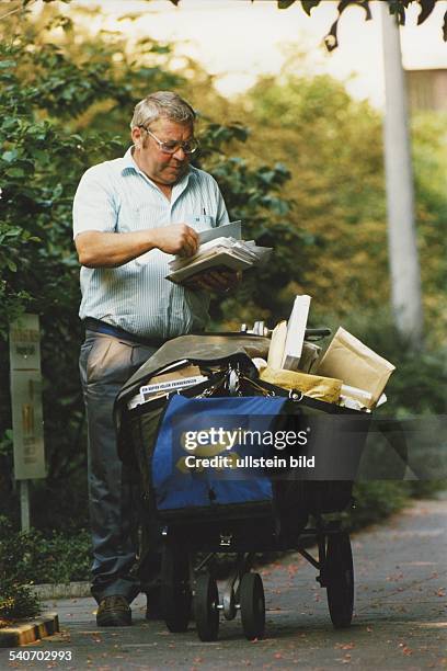 Ein Postbote der Bundespost mit Brief- und Zeitungswagen bei der Arbeit. Aufgenommen Mai 1990.