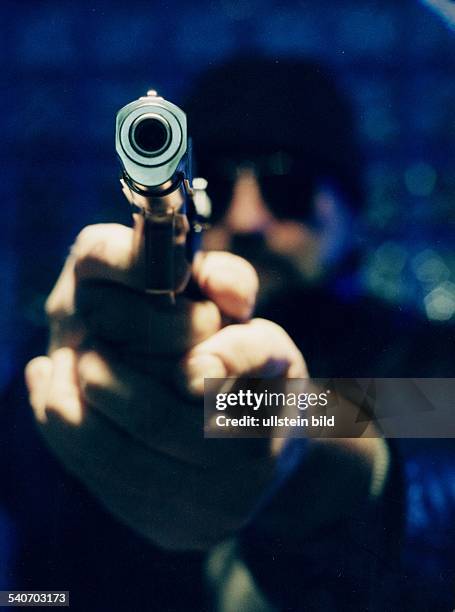 Ein vermummter Mann hält eine großkalibrige Schußwaffe mit beiden Händen. Bedrohung; bedrohen; Gewalt; gezielt; Kriminalität; zielen
