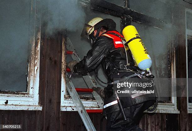 Ein Mann von der Hamburger Feuerwehr klettert mit Atemschutzmaske und Sauerstoffflasche in ein brennendes Haus, aus dem Qualm und Rauch dringt....