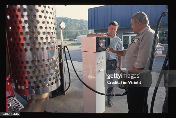 Service station attendant watches and assists a truck driver in using the gas station's new fuel pump.