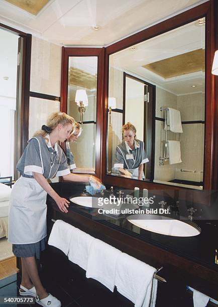 Ein Zimmermädchen im schwarz-weiß gestreiften Kleid mit weißer Schürze im Hotel Adlon in Berlin putzt ein Waschbecken in einem Gästebadezimmer. Vor...