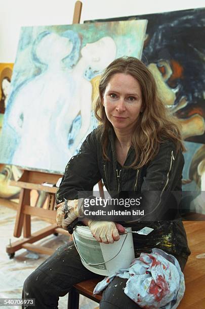 Die Malerin Uta Dellbridge in ihrem Atelier in Hamburg mit einem Farbeimer auf den Knien und einer Staffelei im Hintergrund. .