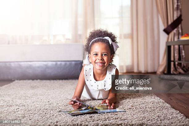 beautiful little girl reading a book on the carpet. - african american baby girls stock pictures, royalty-free photos & images