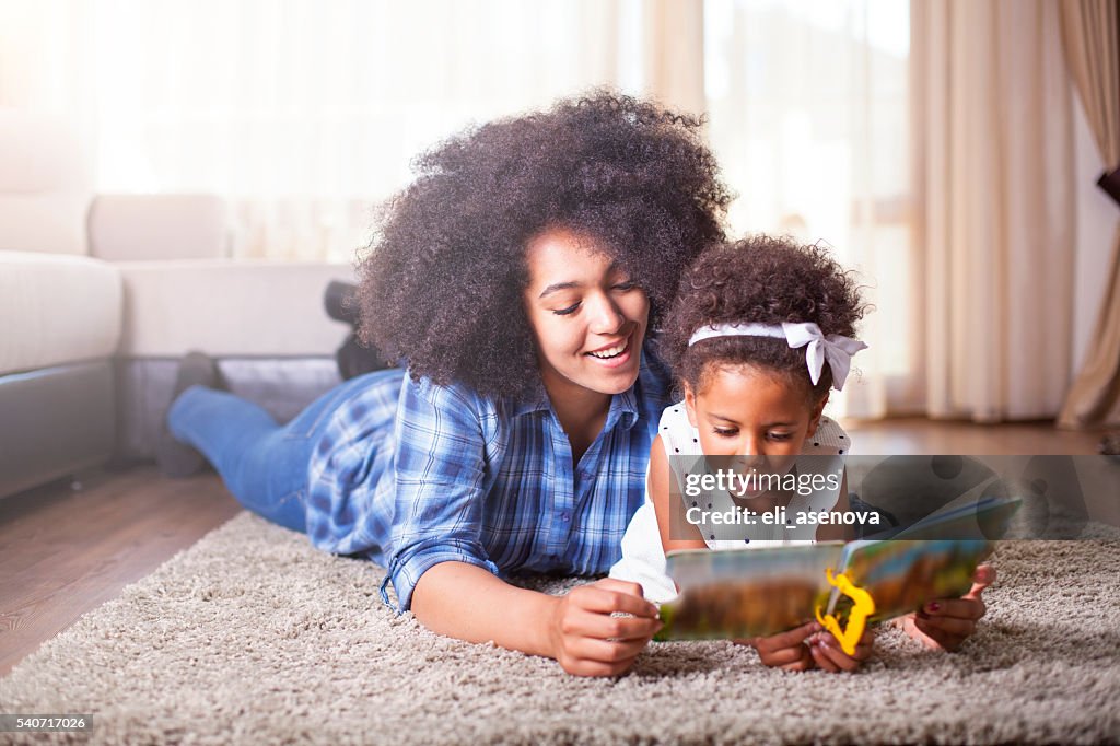 Mutter beim Buchlesen zu Ihrer Tochter auf dem Teppich