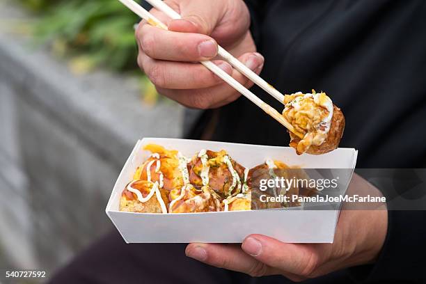 man eating japanese street food with chopsticks, takoyaki octopus balls - straatvoedsel stockfoto's en -beelden