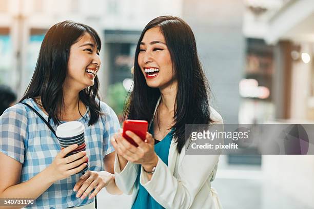 ガールフレンドの席で笑い合うスマートフォンコンテンツ - 若い カワイイ 女の子 日本人 ストックフォトと画像