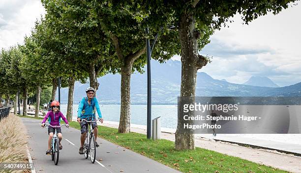 people bike riding along lake - lac d'annecy photos et images de collection