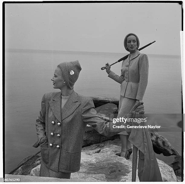 Woman models a tweed box suit by Kraus while another woman models a pinch waist suit by Hattie Carnegie.