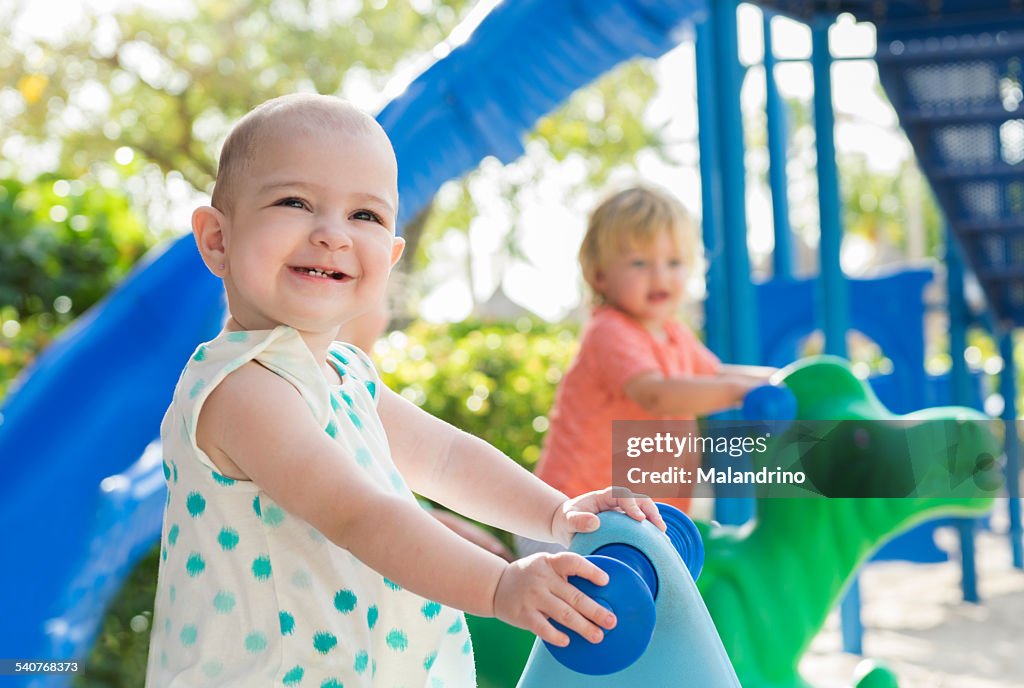 Baby girl and boy riding a toy at the playground