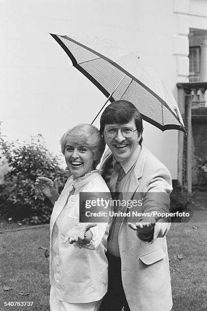 British broadcasters and presenters of the BBC television series Saturday Live, Gloria Hunniford and Simon Bates pictured together under an umbrella...