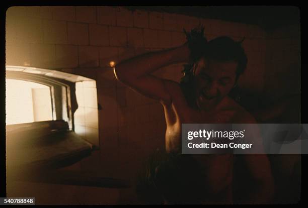 Man in a banya beats himself with 'veniks', . These are used to help fan the heat down from the ceiling and also to increase the circulation.