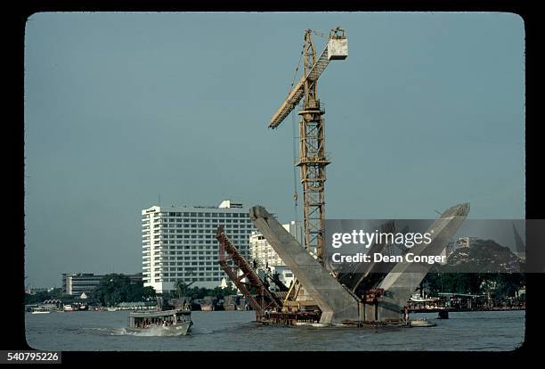 Ferry boat travel the Chao Phraya River near a crane at the construction site for a bridge to connect Bangkok and Thon Buri.