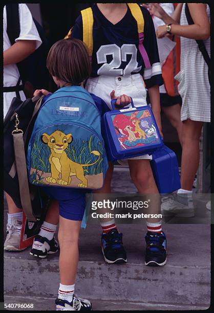 Boy walks with his backpack and lunchbox, which contain cartoon characters from the Disney animation film The Lion King. These children are residents...