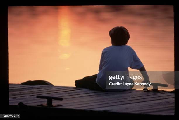 boy sitting on a dock at sunset - isle royale national park - fotografias e filmes do acervo