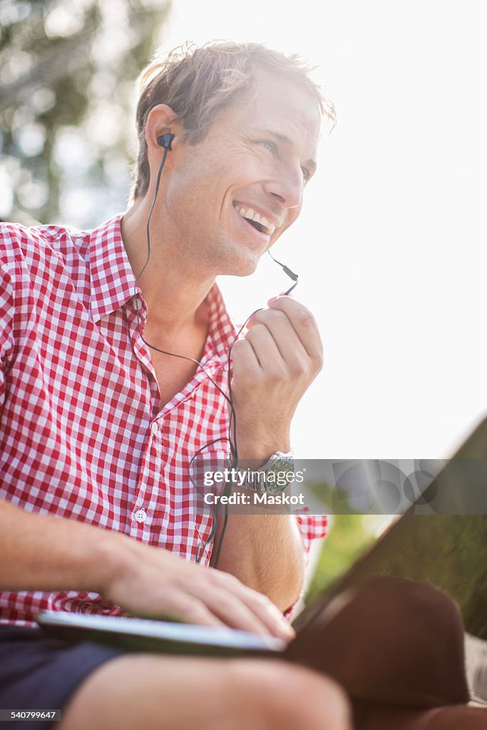 Low angle view of happy man using hands-free device against clear sky