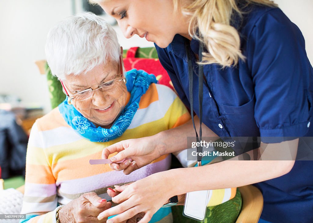 Caretaker filing senior womans fingernails at nursing home