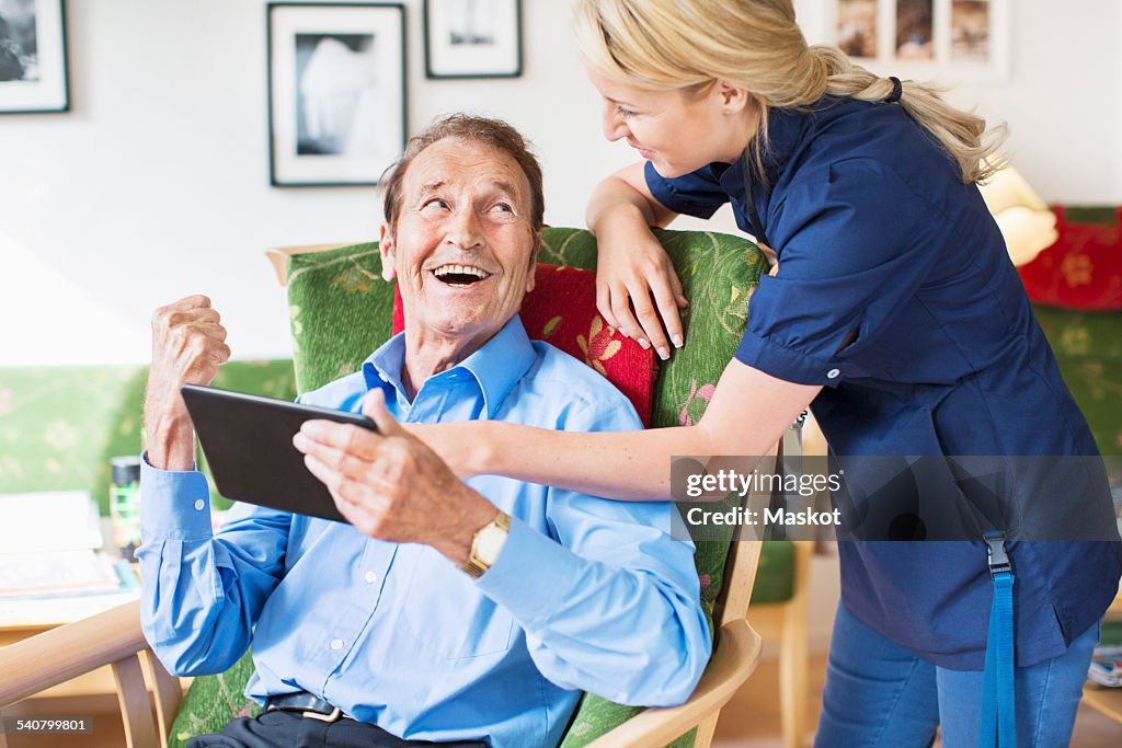 Happy senior man and female caretaker using digital tablet at nursing home