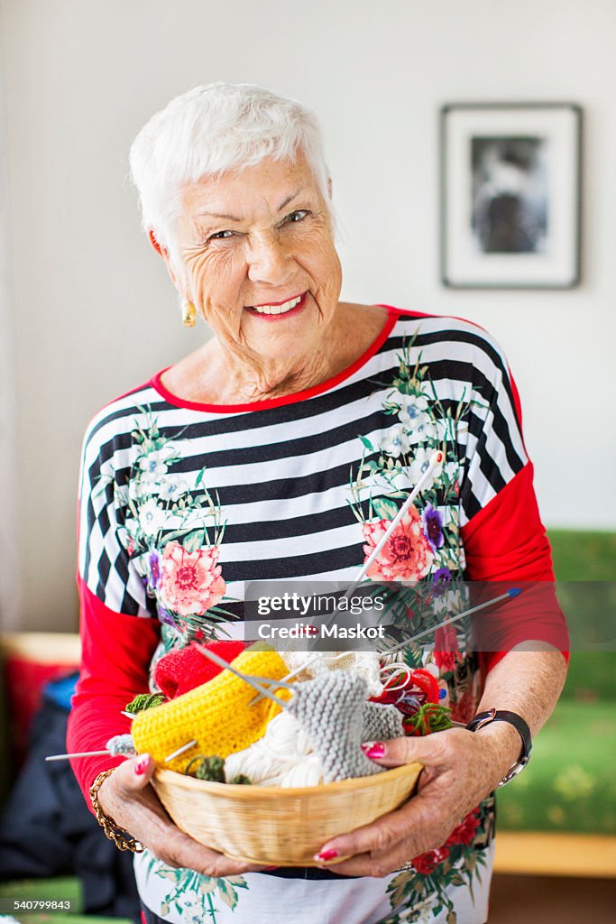 Portrait of happy senior woman holding knitting basket at nursing home