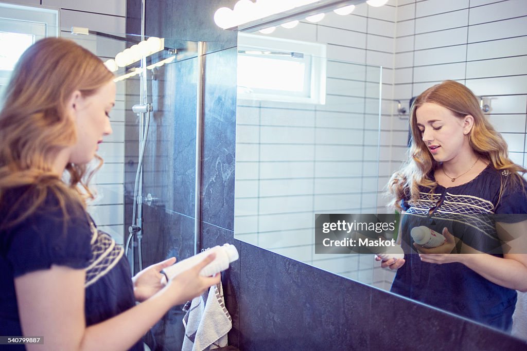 Young woman holding perfume bottles in front of bathroom mirror