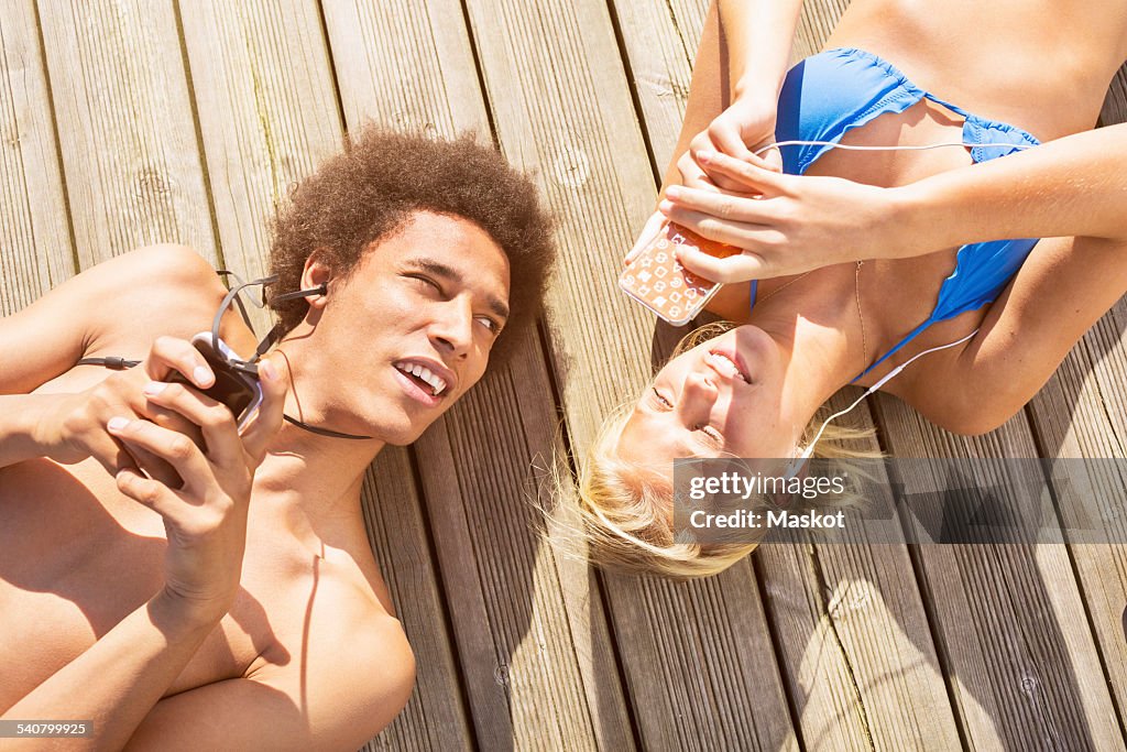 Man looking at woman using smartphone while lying on boardwalk