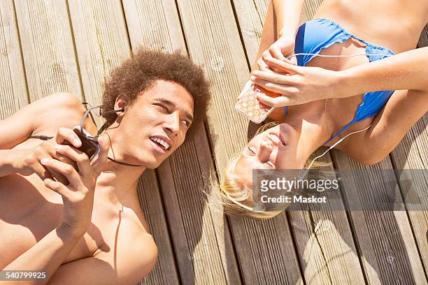 man looking at woman using smartphone while lying on boardwalk - stockholm beach stock pictures, royalty-free photos & images