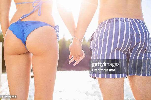 midsection rear view of couple holding hands at lake - womens bottoms stockfoto's en -beelden