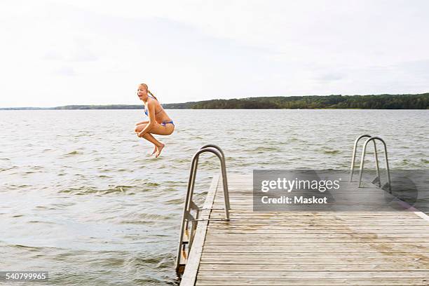 full length side view of excited woman jumping into lake - stockholm beach stock pictures, royalty-free photos & images