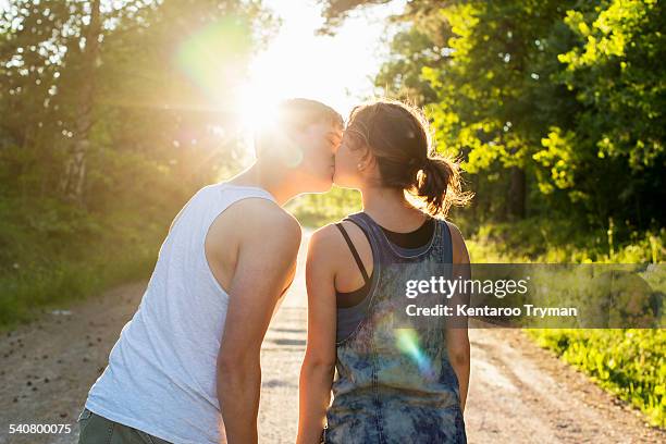 rear view of couple kissing on dirt road against bright sun - sun flare couple stock-fotos und bilder