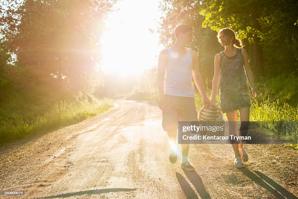 Full length front view of couple walking on dirt road against bright sun