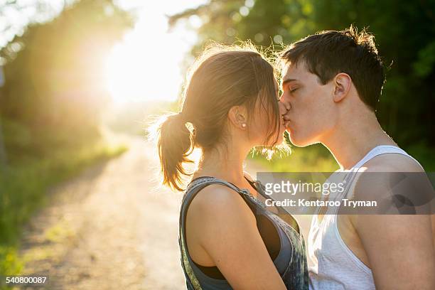 couple kissing on dirt road against bright sun - sun flare couple stock-fotos und bilder
