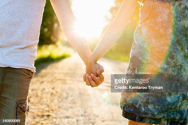 midsection of couple holding hands on dirt road against bright sun - sun flare couple stock-fotos und bilder