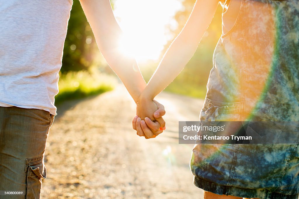 Midsection of couple holding hands on dirt road against bright sun