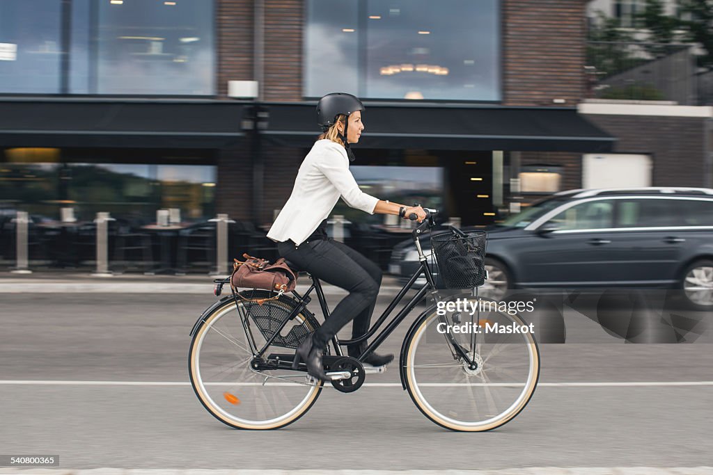 Full length of businesswoman riding bicycle on city street